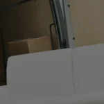 Weiße Couch wird von zwei Möbelpackern in einen LKW verladen